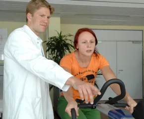 Arzt begleitet eine Patientin beim Belastungstest auf einem Fahrradergometer.